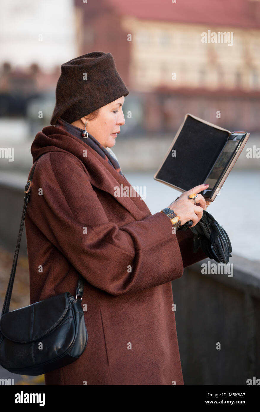 La donna in un cappotto marrone e il cappello con una tavoletta digitale sta con il suo indietro Foto Stock
