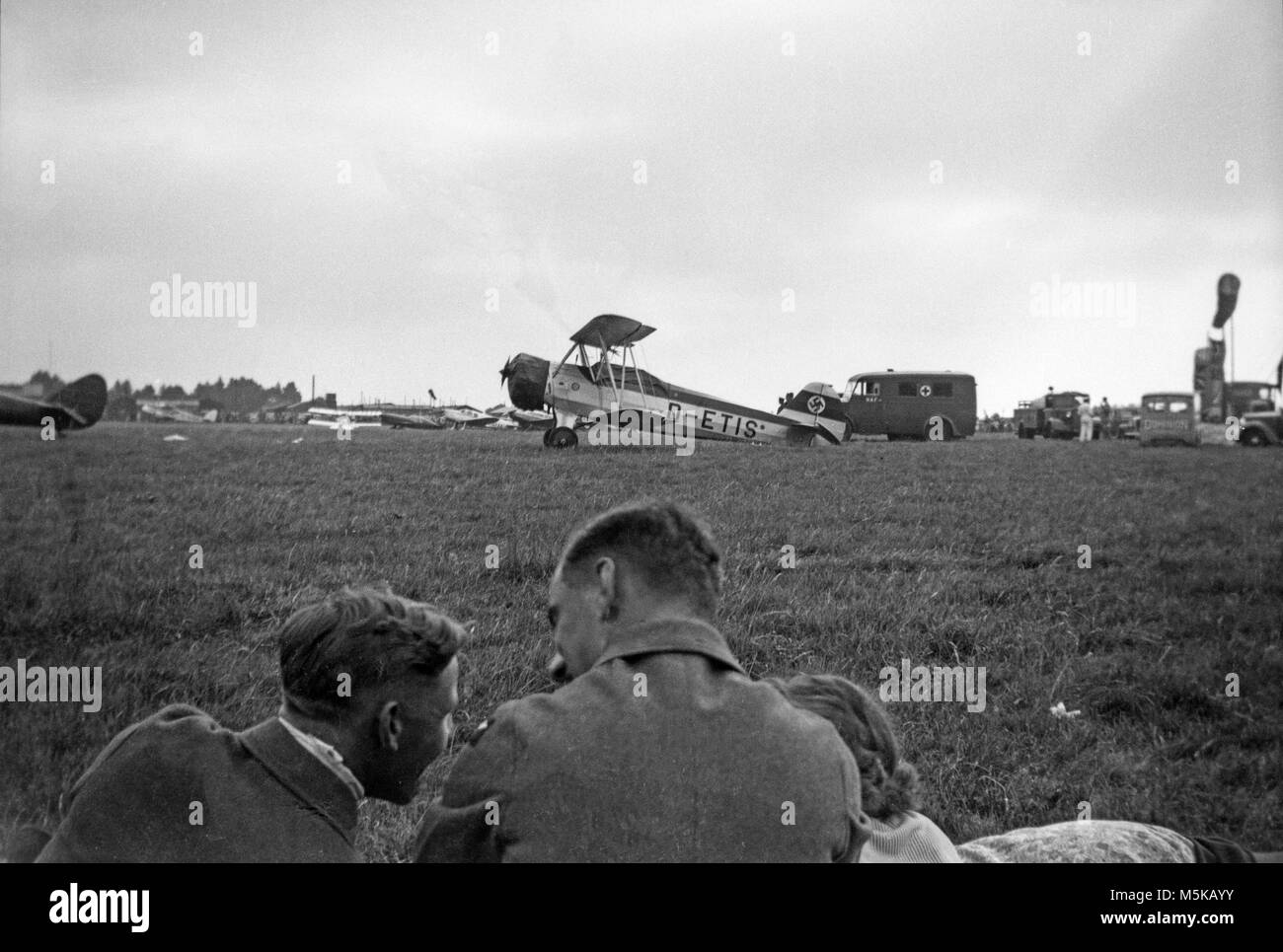 Un 1930 fotografia mostrante un Focke-Wulf FW44, D-ETIS, con un emblema con la svastica sulla coda, a uno sconosciuto Aviosuperficie europea. Molti altri aerei possono essere visti sullo sfondo. Due uomini in uniforme militare, e di una donna, sono in primo piano. Foto Stock