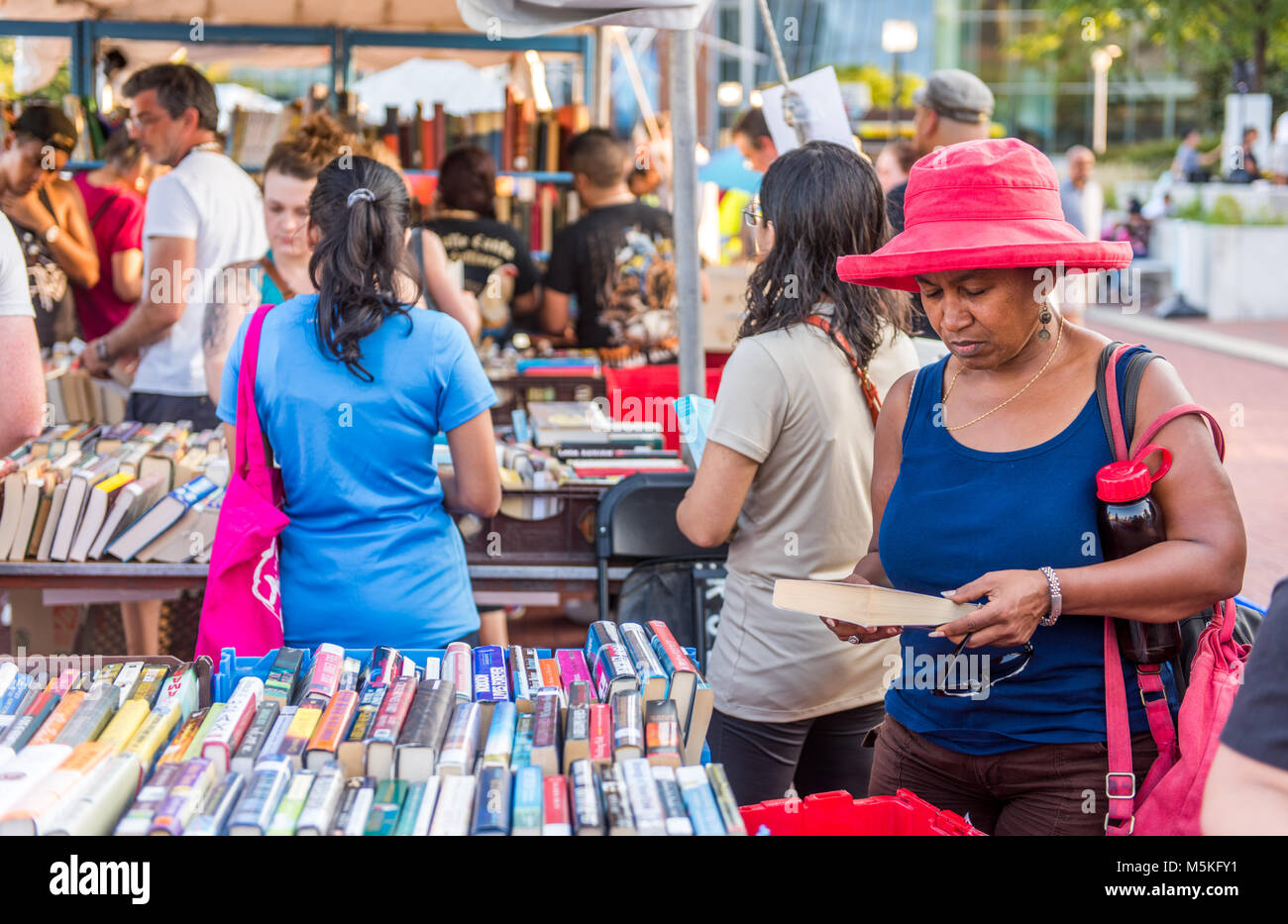 African American donna legge torna di nuovo mentre altri individui navigare attraverso le casse piene di libri per la vendita, Baltimore, Maryland. Foto Stock