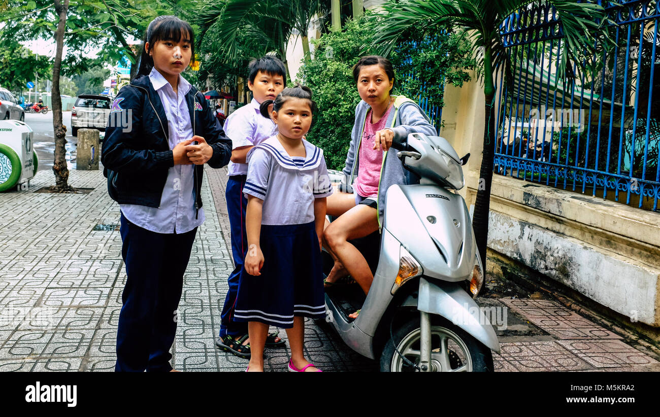 A scuola i bambini guardano inquisitively mentre seduto su un ciclomotore in Vietnam Foto Stock