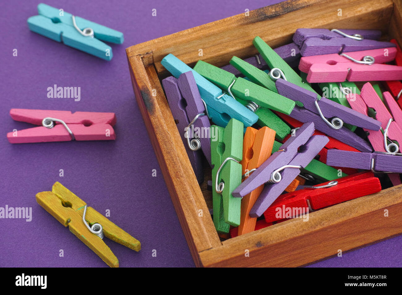 Clothespins colorati in una scatola di legno su sfondo viola. Close up. Foto Stock