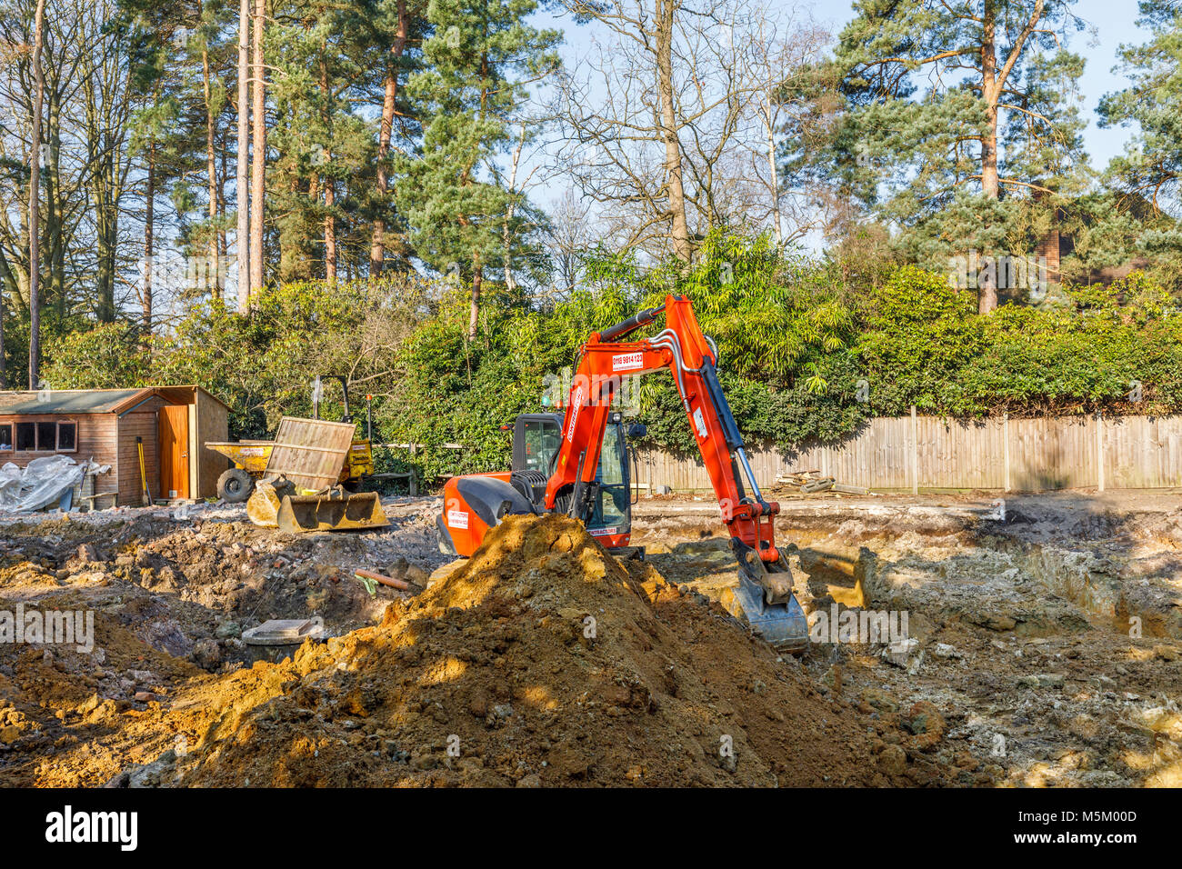 Arance grandi impianti pesanti escavatore meccanico parcheggiato su un cantiere di scavo dopo gli scavi per le fondazioni di un nuovo sviluppo residenziale Foto Stock