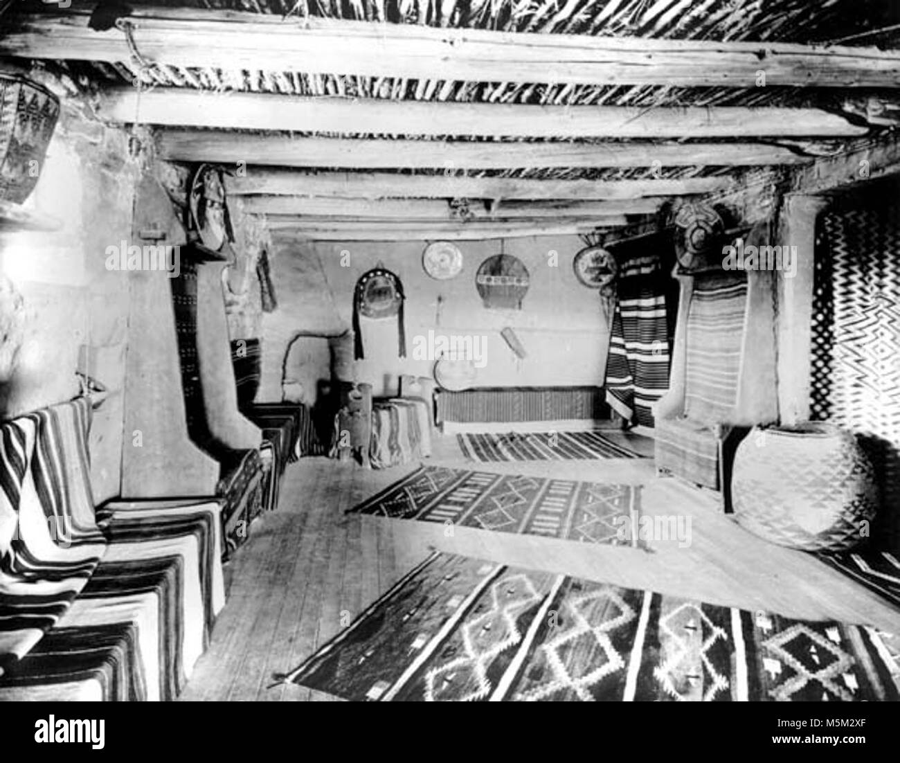 Grand Canyon Hopi storico interno di una casa c . Al piano superiore camera di vendita in hopi house. Panche intorno a camera drappeggiati con tappeti navajo. Circa 1905. Foto Stock