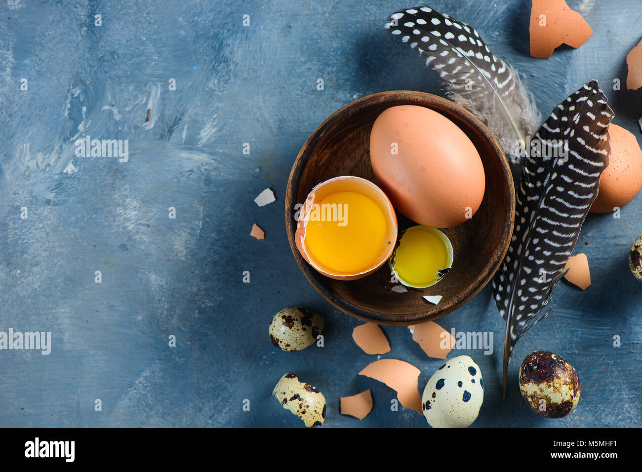 Tuorlo d'uovo in un guscio d'uovo close-up. Materie di cottura Ingredienti sfondo con copia spazio. Moderno concetto di Pasqua marrone con uova di gallina e piume Foto Stock