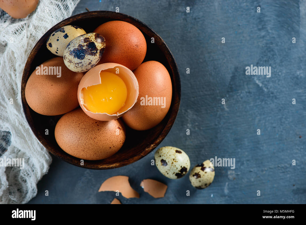 Testata con materie brown hen e uova di quaglia, intere e rotte, su un piatto di legno. Sfondo di calcestruzzo con copia spazio. Moderno concetto di Pasqua. Foto Stock