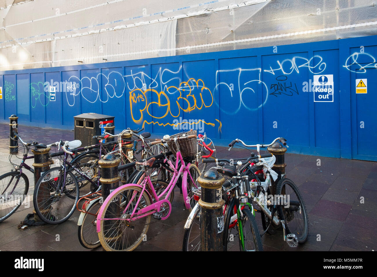 Biciclette concatenati per Rastrelliere per biciclette su un marciapiede davanti al sito in costruzione cartelloni coperto di graffiti tag nel centro di Cardiff Galles. Foto Stock