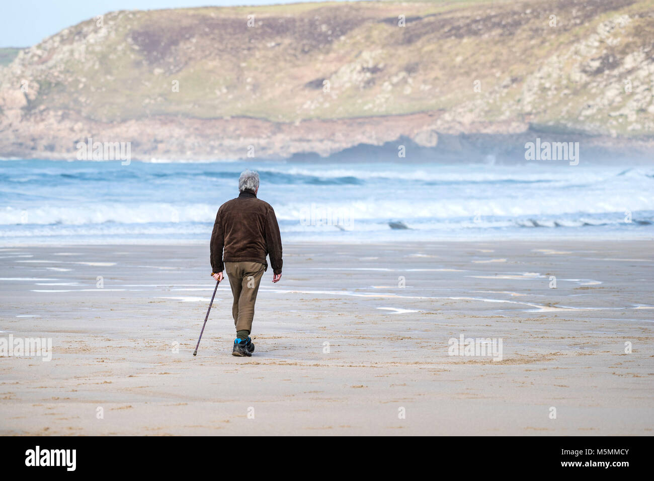 Un uomo che cammina attraverso la spiaggia di Sennen Cove in Cornovaglia. Foto Stock