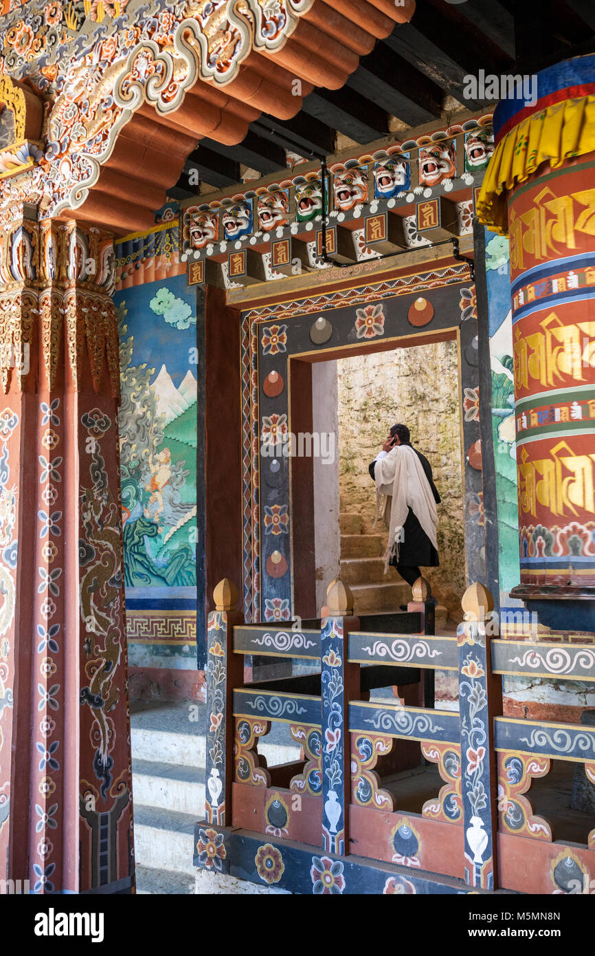 Trongsa, Bhutan. Uomo in abito tradizionale (Gho) entrando in un cortile interno in Trongsa Dzong (Monastery-Fortress). Ruota di preghiera a fianco Entra Foto Stock