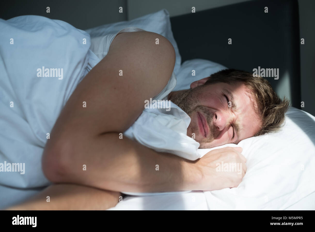 Caucasian uomo maturo in t-shirt bianco non vuole alzarsi al mattino Foto Stock