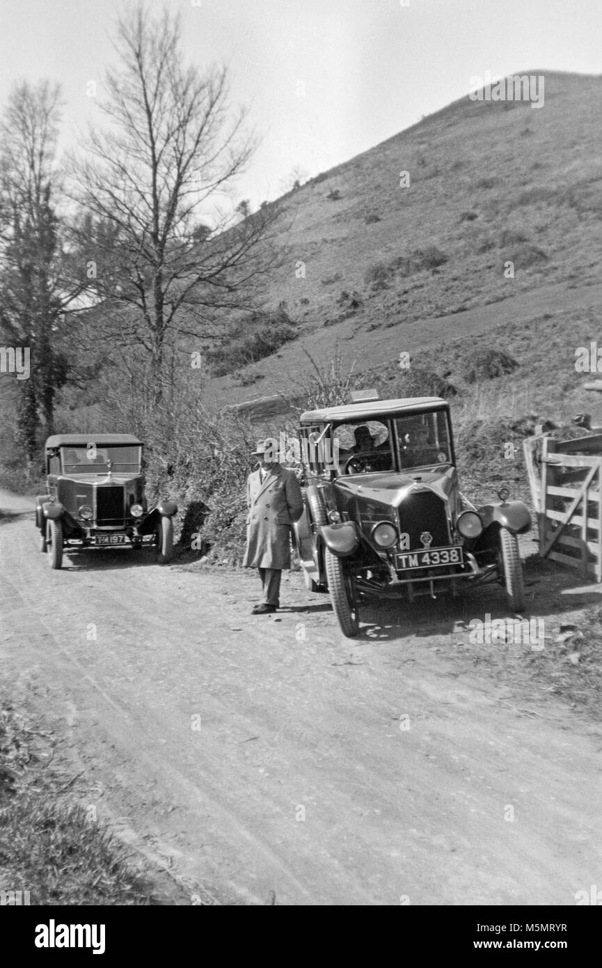 Contemporary in bianco e nero 1920s immagine delle due vetture vintage parcheggiata da un lato di una piccola strada nella campagna britannica. Foto Stock