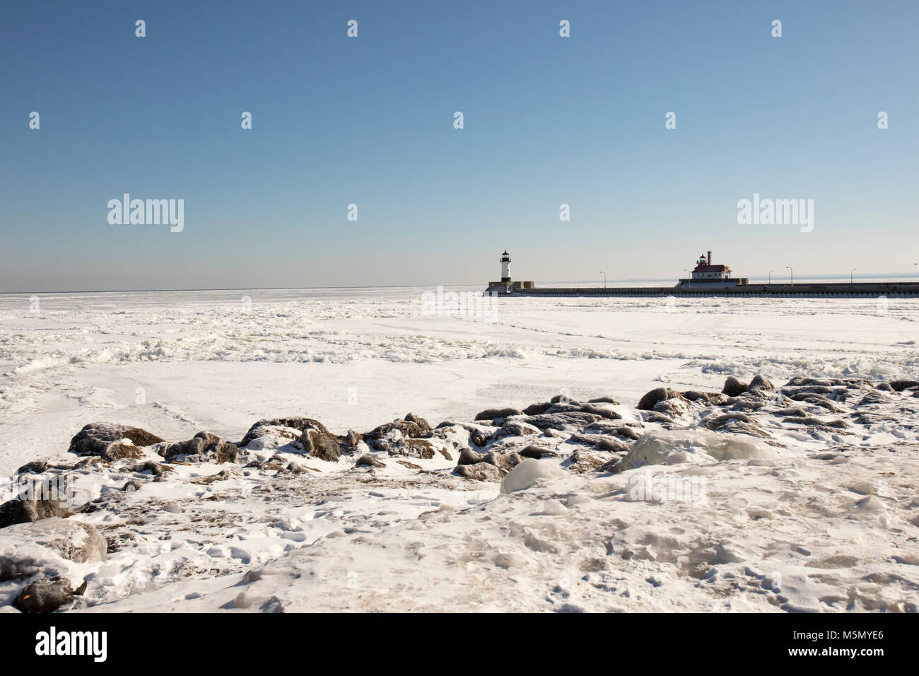 Coperte di ghiaccio sponde rocciose del lago ghiacciato Superior accanto al molo lungo il canale di spedizione con fari a Duluth, Minnesota, Stati Uniti d'inverno. Foto Stock