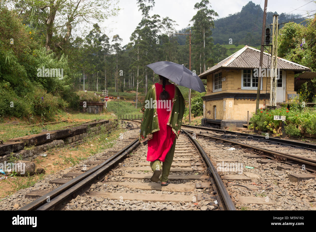Donna che indossa tradizionale sari e Ombrello nero a camminare su binari ferroviari in Sri Lanka. Foto Stock