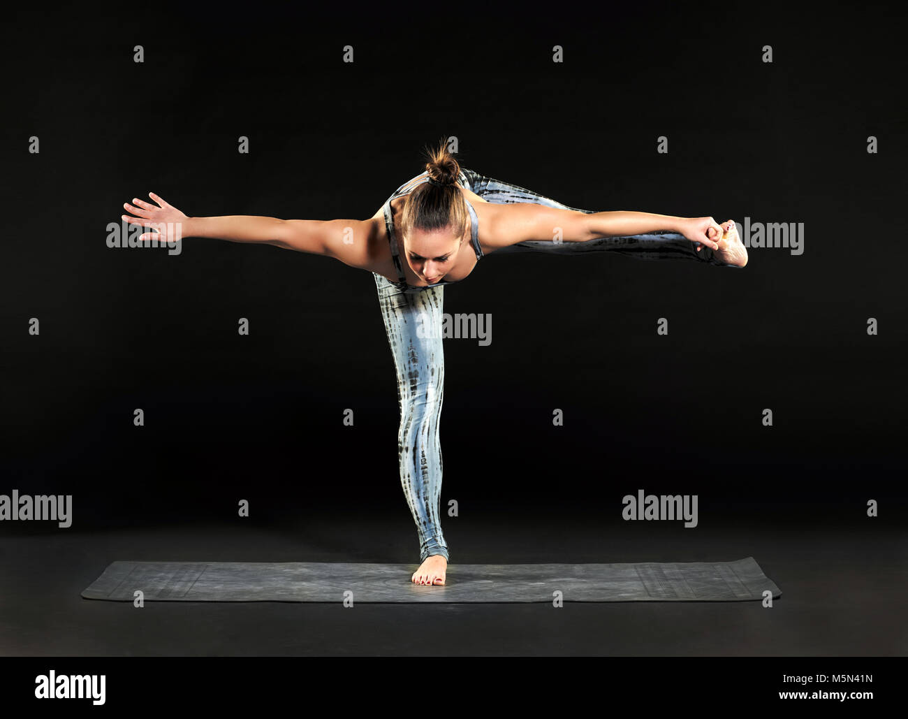 Donna facendo esercizi di bilanciamento durante un allenamento di yoga che adotta una mano a alluce permanente equilibrio pongono su una gamba sola con le braccia tese e gamba sopra Foto Stock