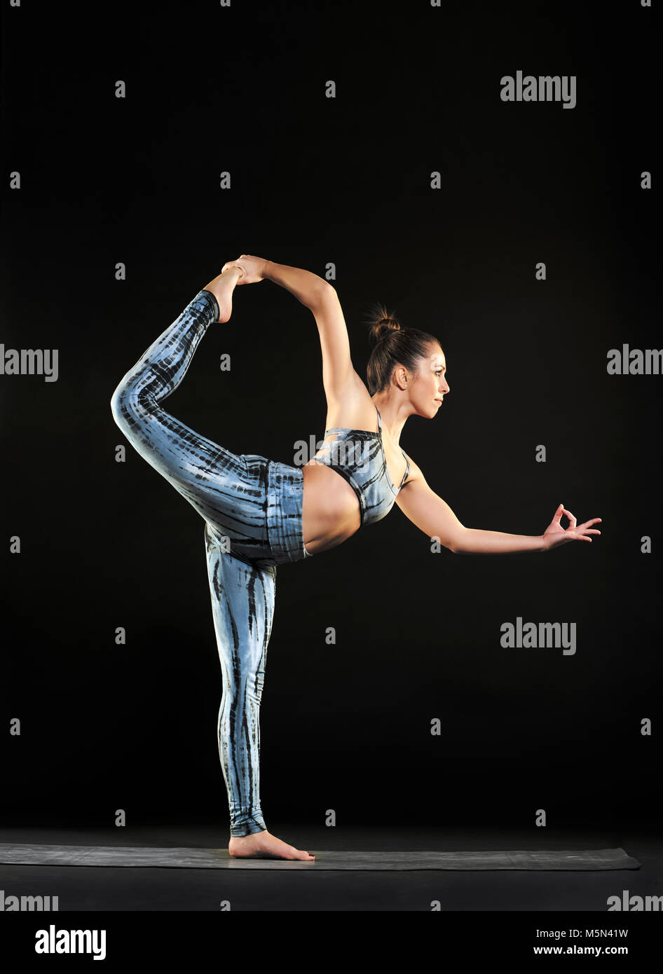 Donna facendo una posizione del signore della danza durante un allenamento di yoga in equilibrio su una gamba sola con gli altri tenendo sollevata una graziosa posizione , vista laterale sul nero con cop Foto Stock