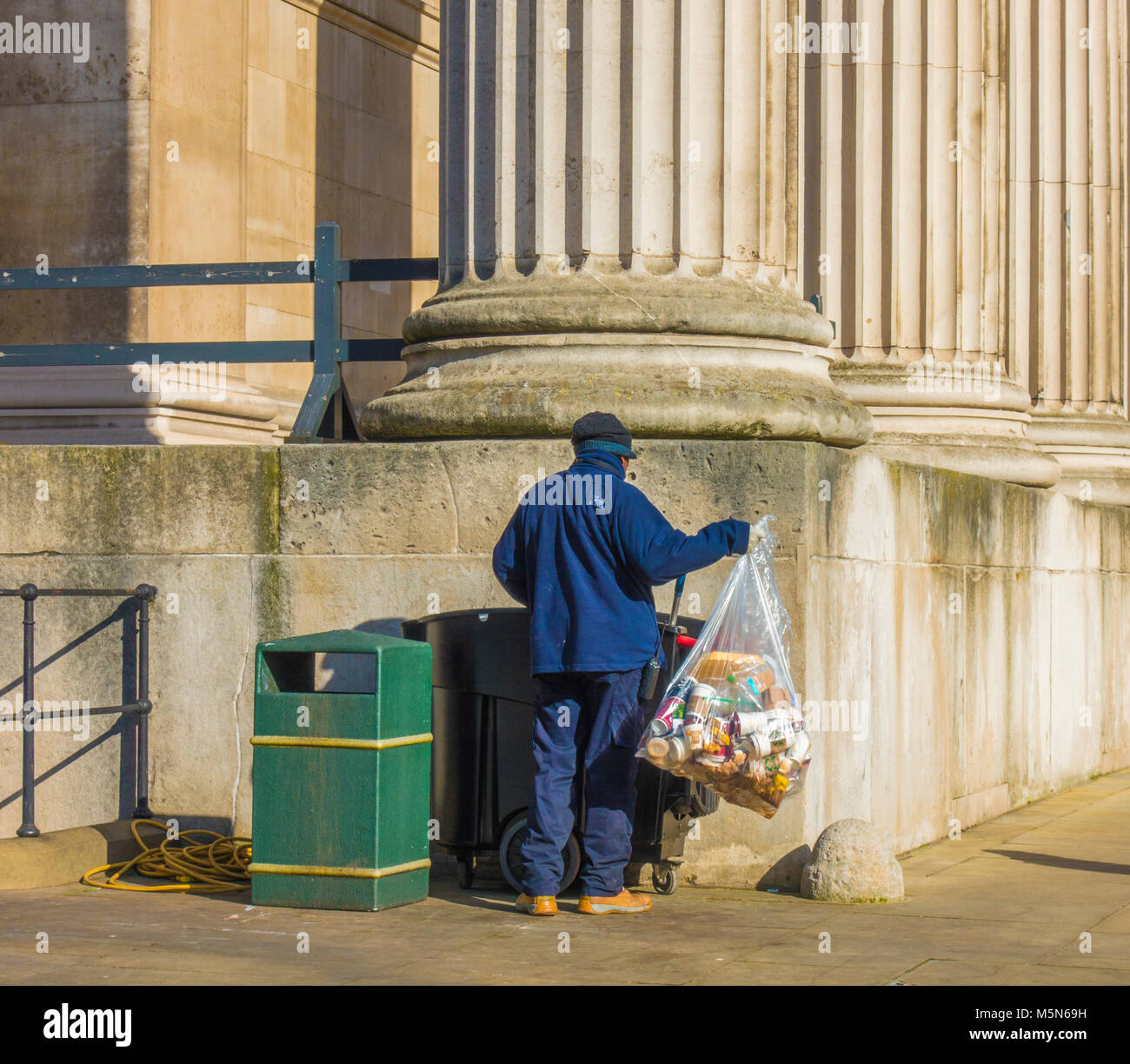 Lavoratore di Londra al di fuori del British Museum, il sollevamento di un contenitore pieno di sacchetto principalmente tazze monouso, per mettere in un recipiente con ruote. Londra, Inghilterra, Regno Unito. Foto Stock