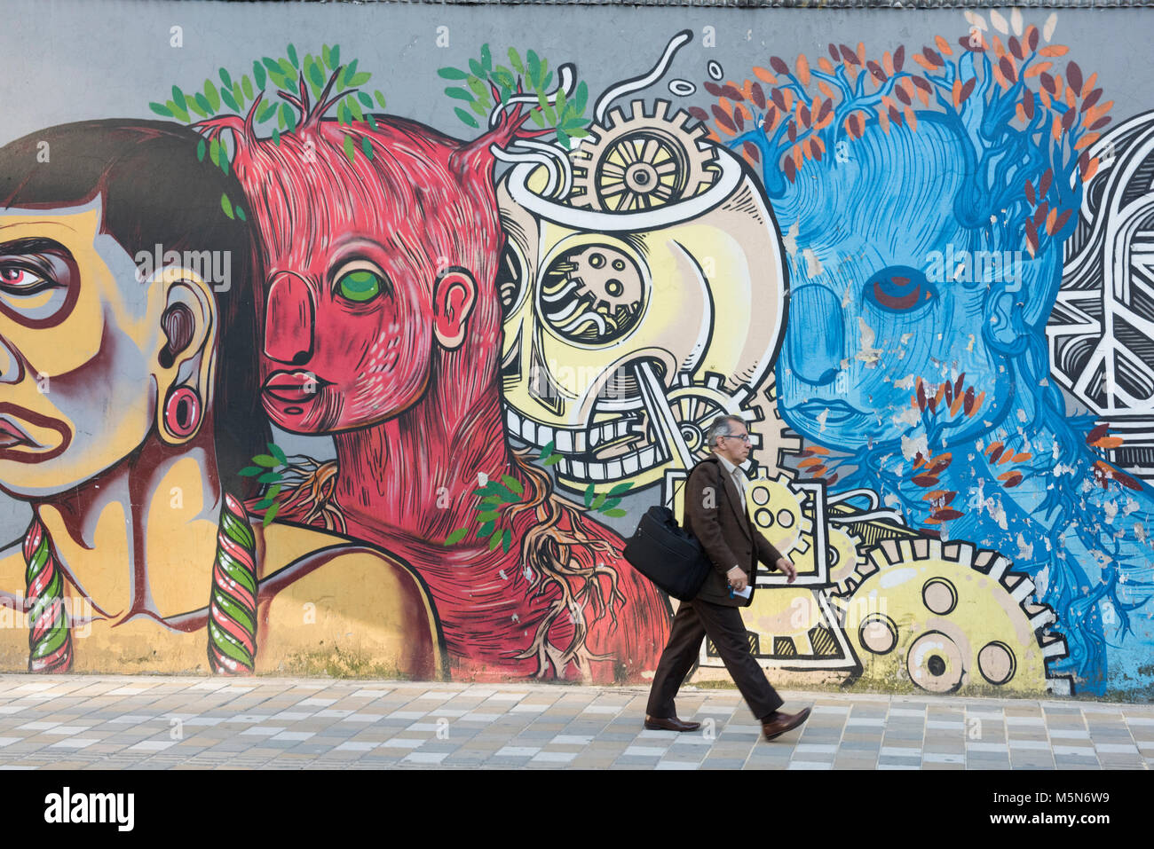 Un colombiano uomo cammina davanti a un muro di graffiti. Graffiti decorano molti spazi pubblici a Bogotà il capitale della Colombia Foto Stock