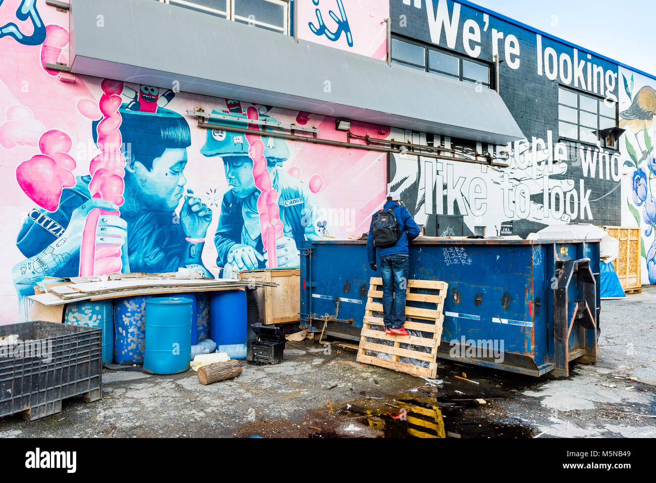 Murale e uomo cerca nel cassonetto, False Creek appartamenti, Vancouver, British Columbia, Canada. Foto Stock