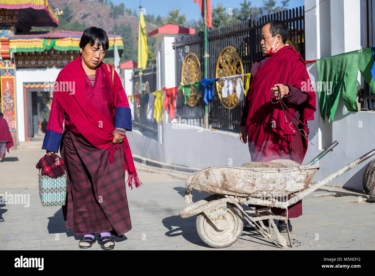 Thimphu, Bhutan. Monaco in piedi dalla carriola con incenso, Donna in abito tradizionale avvicinando Grande Buddha Dordenma statua. Foto Stock