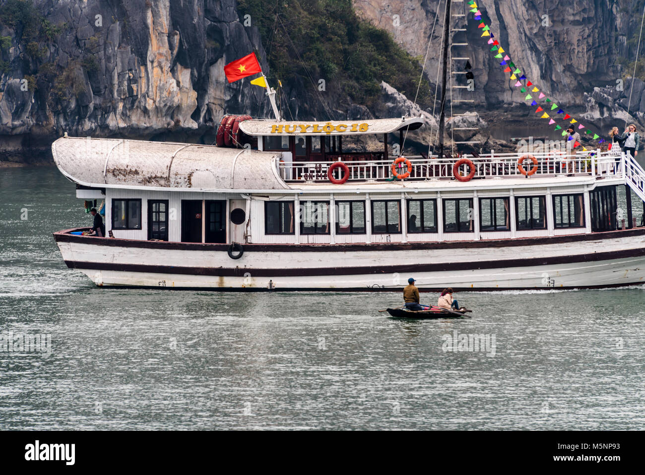 Di trasporto turistico di passeggeri della nave di crociera vele davanti a due pescatori in una piccola barca a remi a Halong Bay, Vietnam Foto Stock