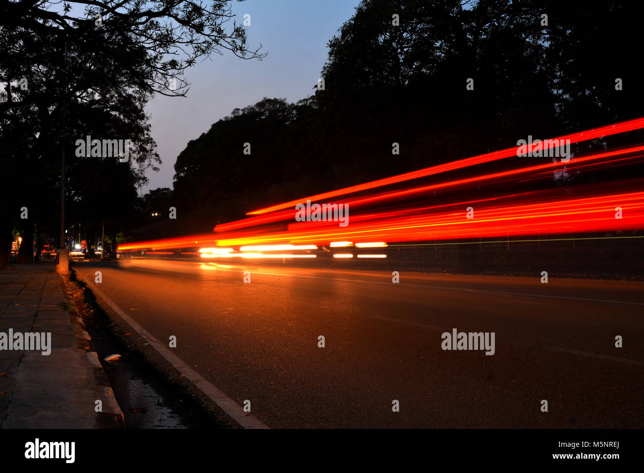 Una lunga esposizione del cielo della sera con alberi e stabile su strada e lo spostamento delle luci auto in movimento creando un bel contrasto nell'immagine. Foto Stock