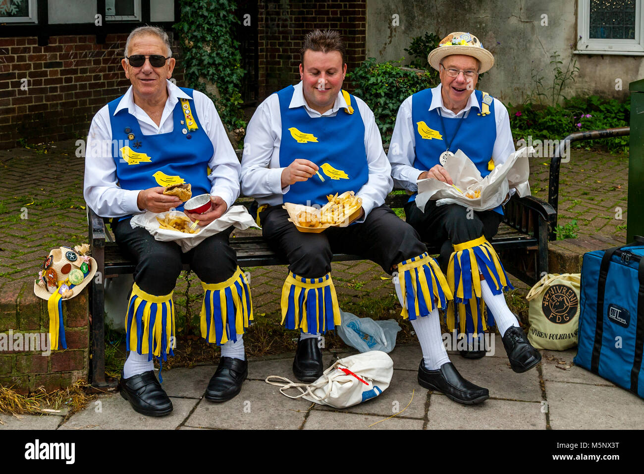 Un gruppo di uomini di Morris a sedersi su una parete di mangiare pesce e patatine durante l annuale Lewes Folk Festival, Lewes, Sussex, Regno Unito Foto Stock