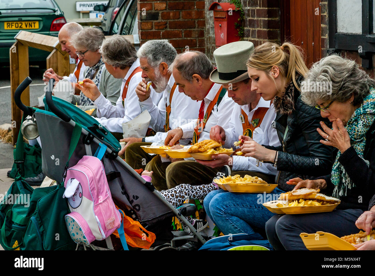 Un gruppo di ballerini di Morris a sedersi su una parete di mangiare pesce e patatine durante l annuale Lewes Folk Festival, Lewes, Sussex, Regno Unito Foto Stock