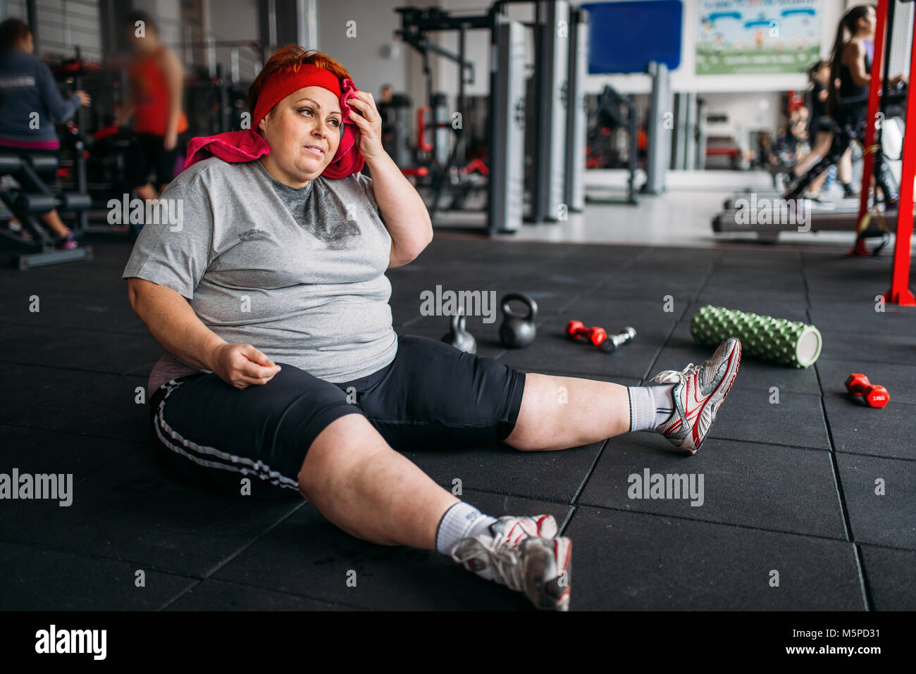 Stanco donna grassa si siede sul pavimento in palestra. Calorie bruciare, femmina obesi in persona lo sport club Foto Stock