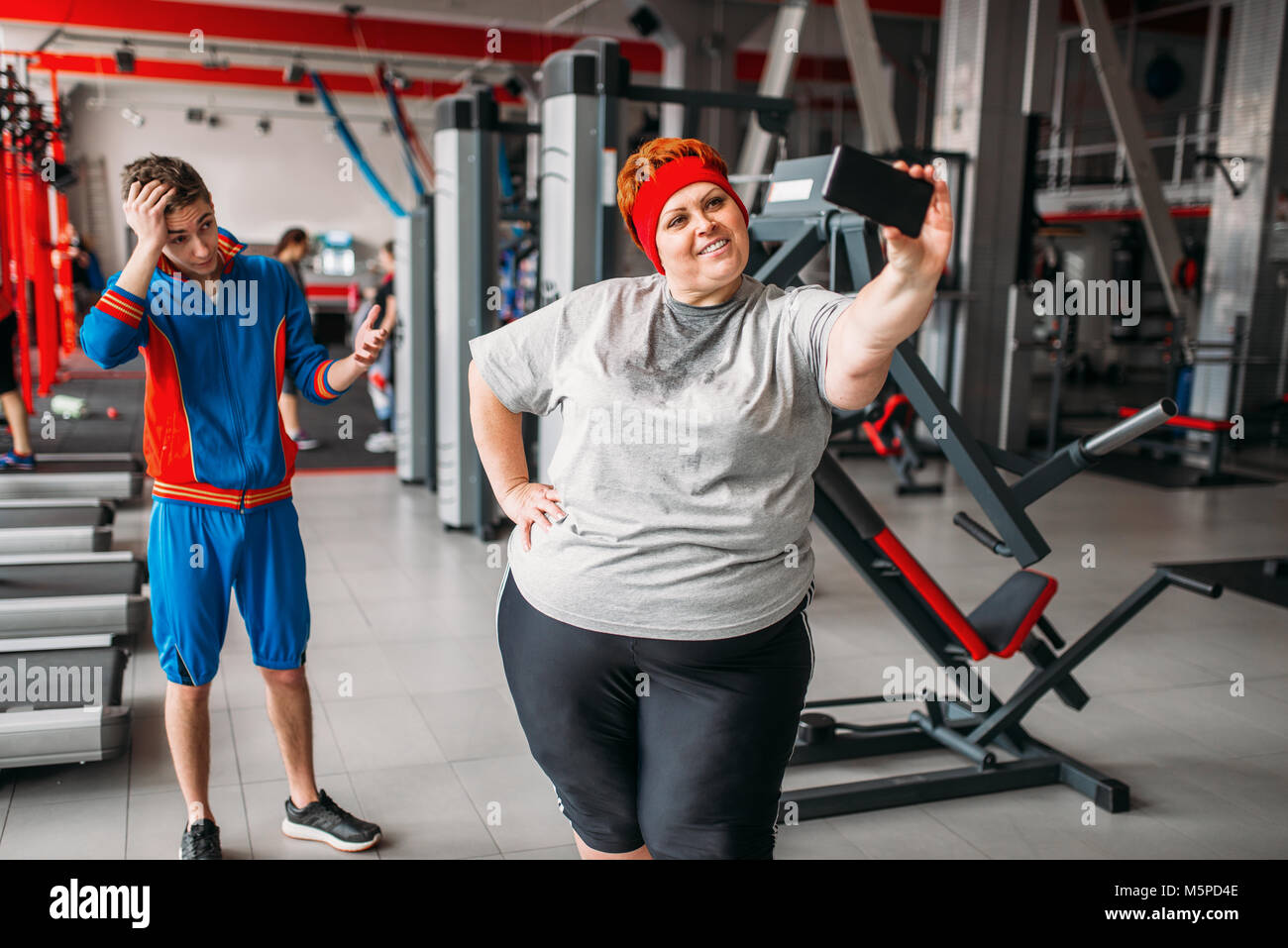 Donna grassa rende selfie con istruttore in palestra, umorismo. Calorie bruciare, femmina obesi in persona lo sport club, fat-burning Foto Stock