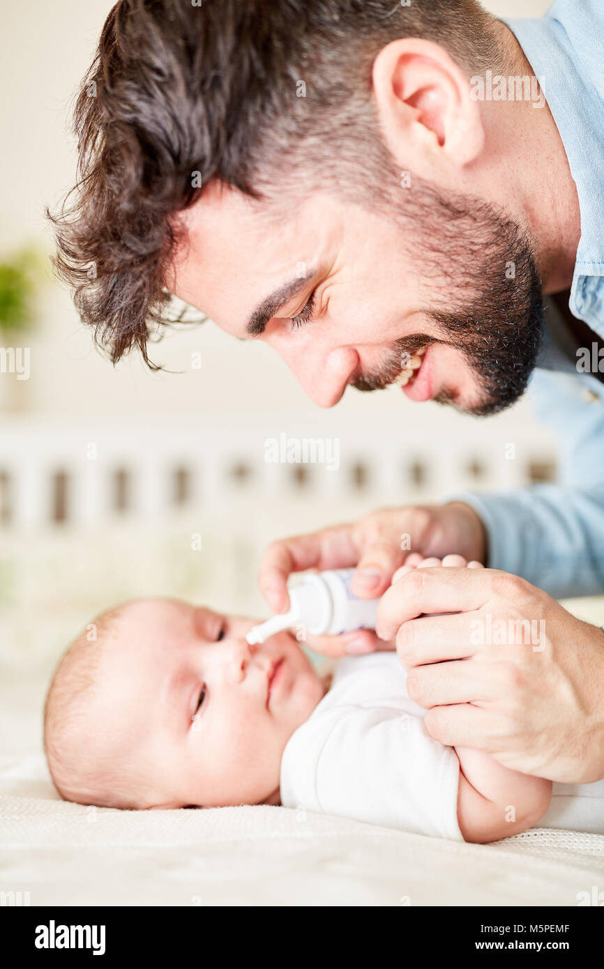 Padre al baby care fornisce il suo bambino spray nasale per raffreddore Foto Stock