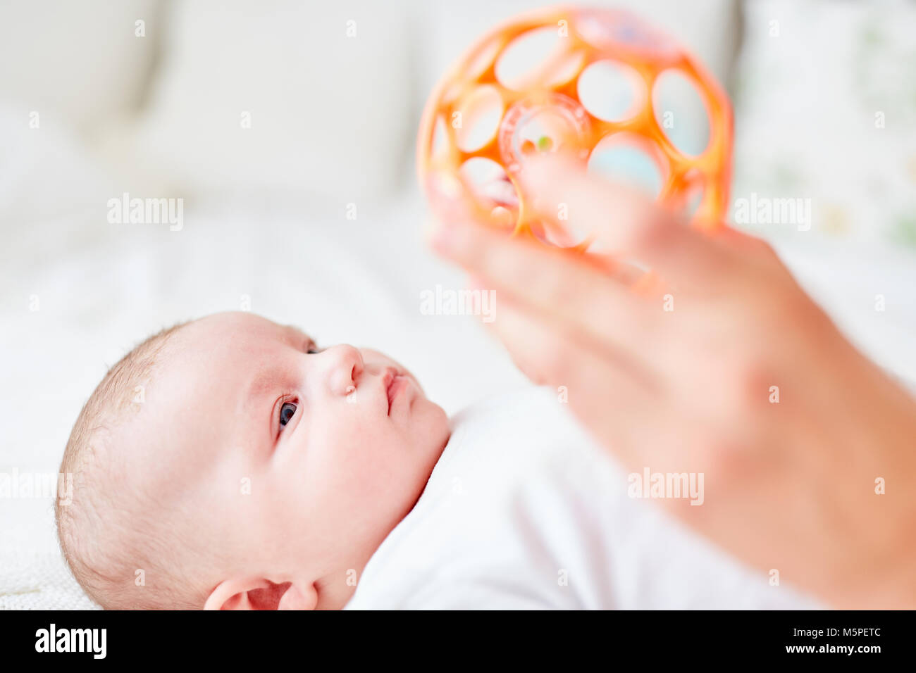 Piccolo bambino si trova sulla sua schiena e guarda al sonaglio palla in mano Foto Stock