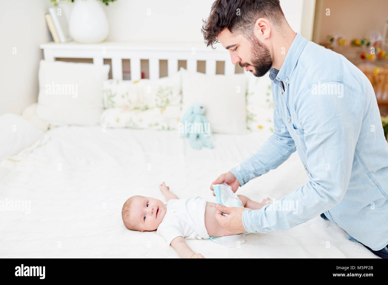 Giovane uomo come Padre in congedo parentale cambia i pannolini del suo bambino Foto Stock