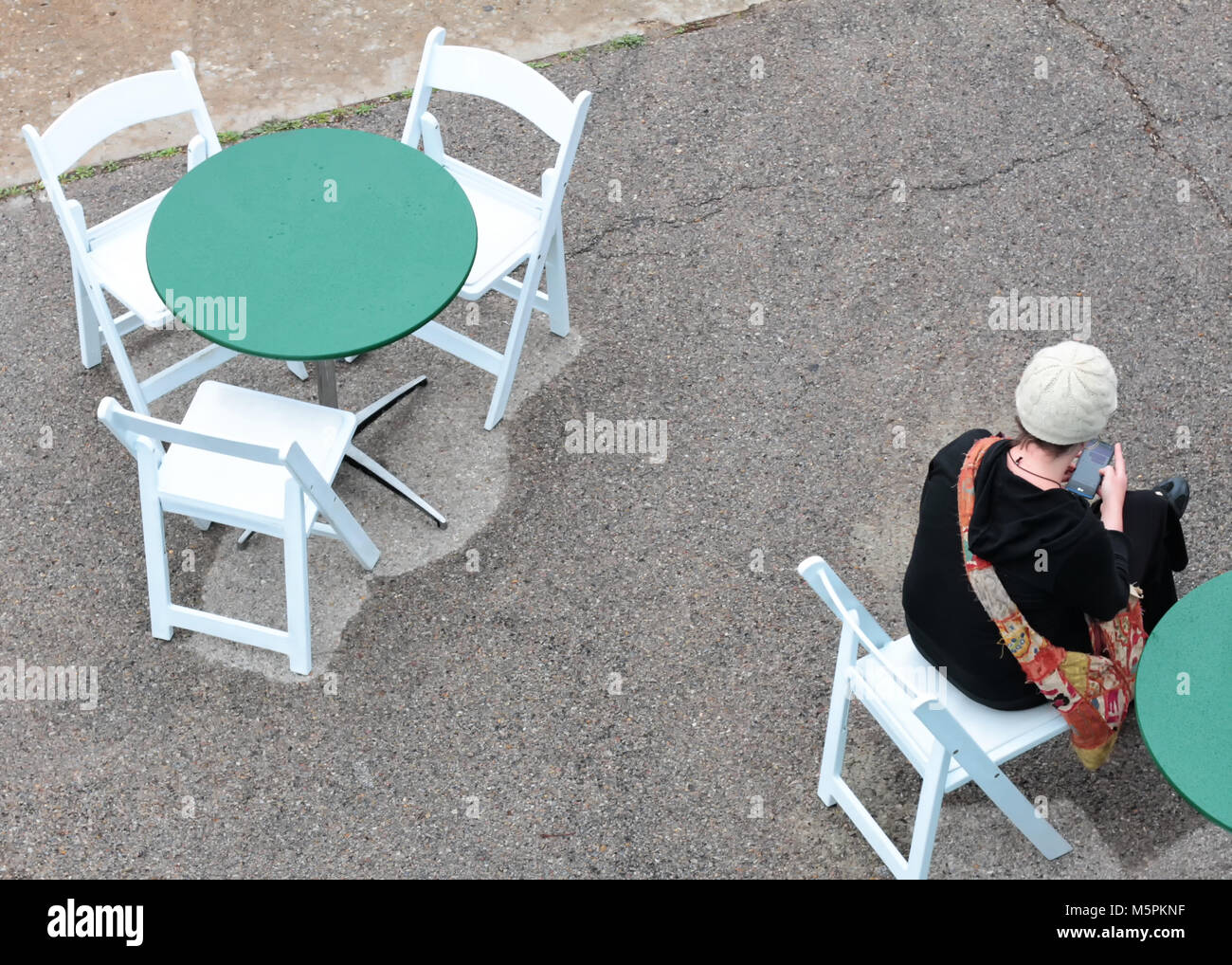 Una giovane donna siede a un outdoor cafe tabella da solo mentre si verifica il suo telefono. Foto Stock