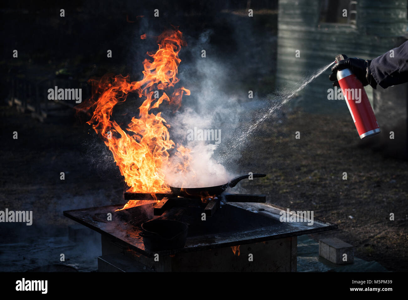 Uomo di spegnere l'incendio in una padella di ferro con schiuma da una bomboletta spray, dimostrazione durante un incendio dipartimento formazione, sfondo scuro con spazio di copia Foto Stock