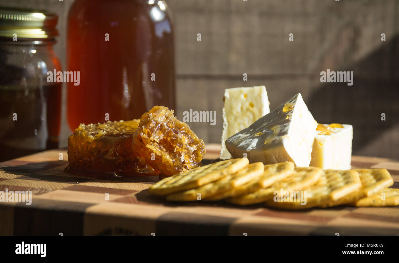 Gourmet Snack-Brie sano formaggio spruzzata con materie di miele, servita con cracker, miele pettine o a nido d'ape visualizzata a lato Foto Stock