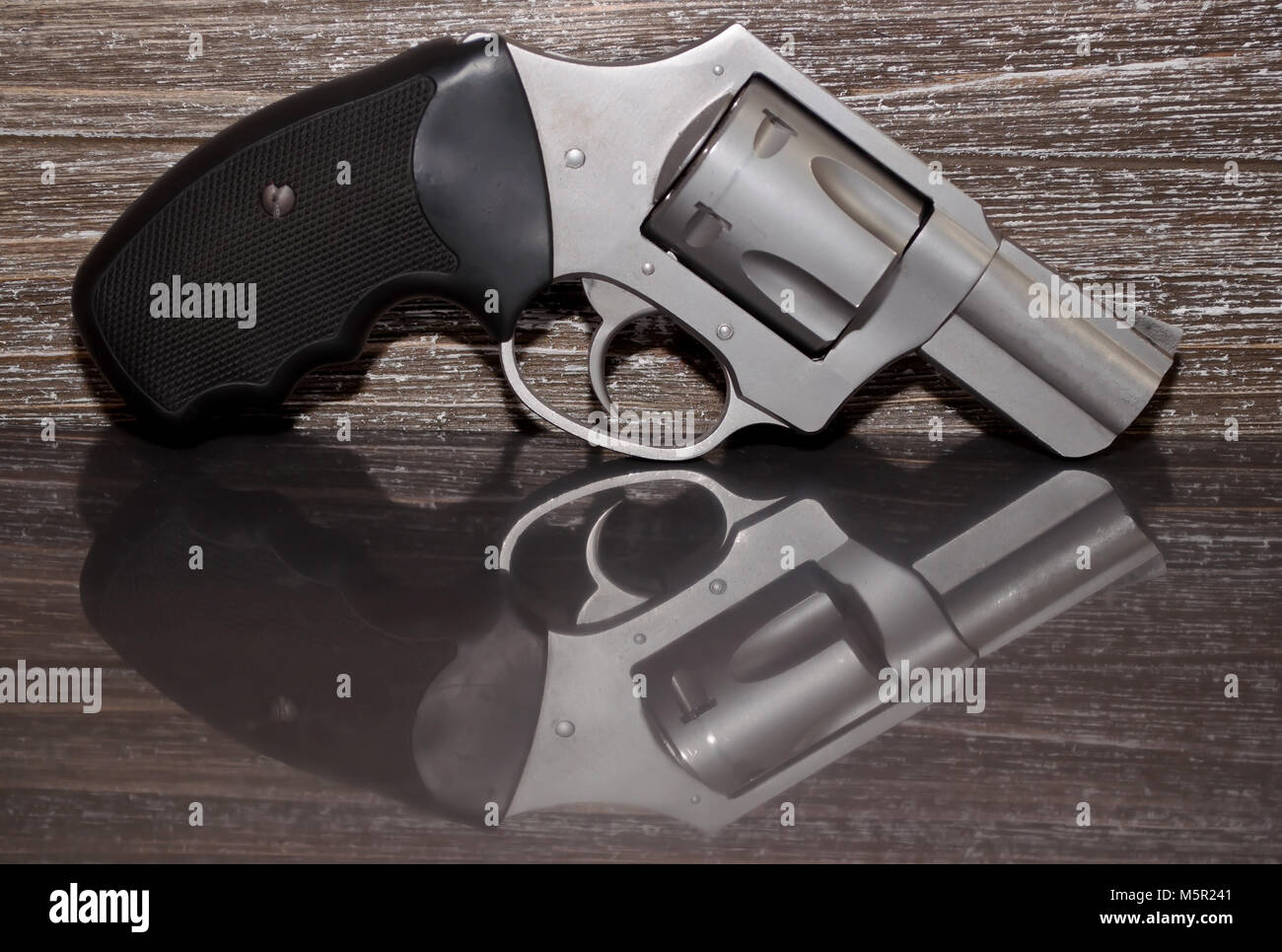 Un acciaio inossidabile .357 revolver Magnum su una superficie riflettente con un background in legno Foto Stock