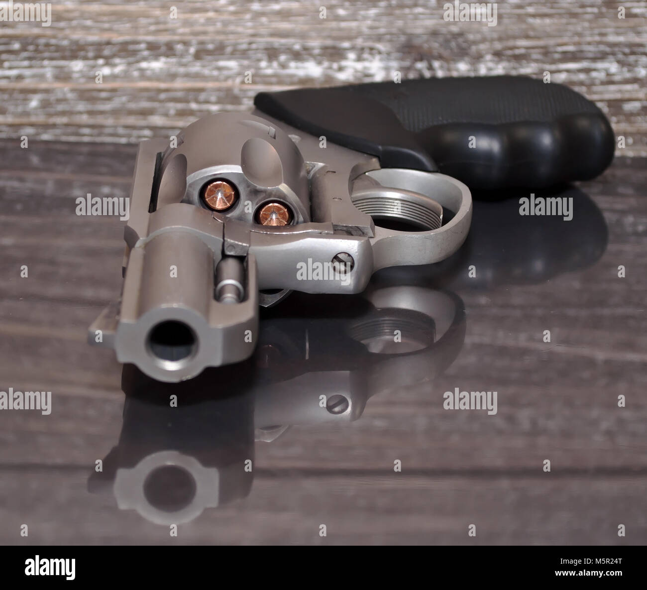Un caricato, acciaio inossidabile .357 revolver Magnum su una superficie riflettente con un background in legno Foto Stock