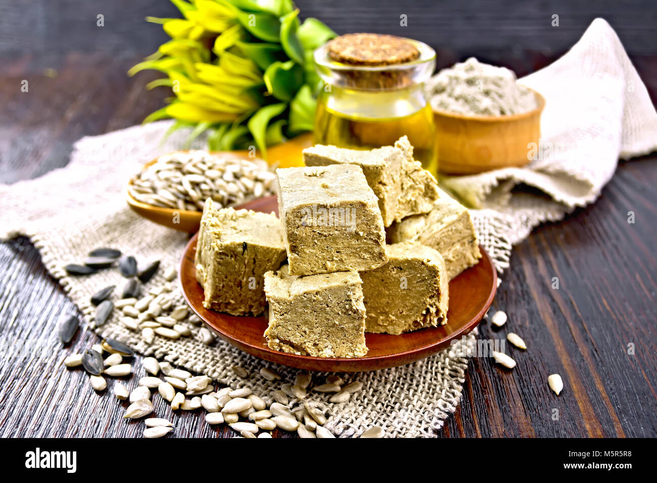 Dolce orientale halva girasole in una piastra, semi di girasole, olio, la farina e il fiore di un saccheggio su uno sfondo di legno scuro board Foto Stock