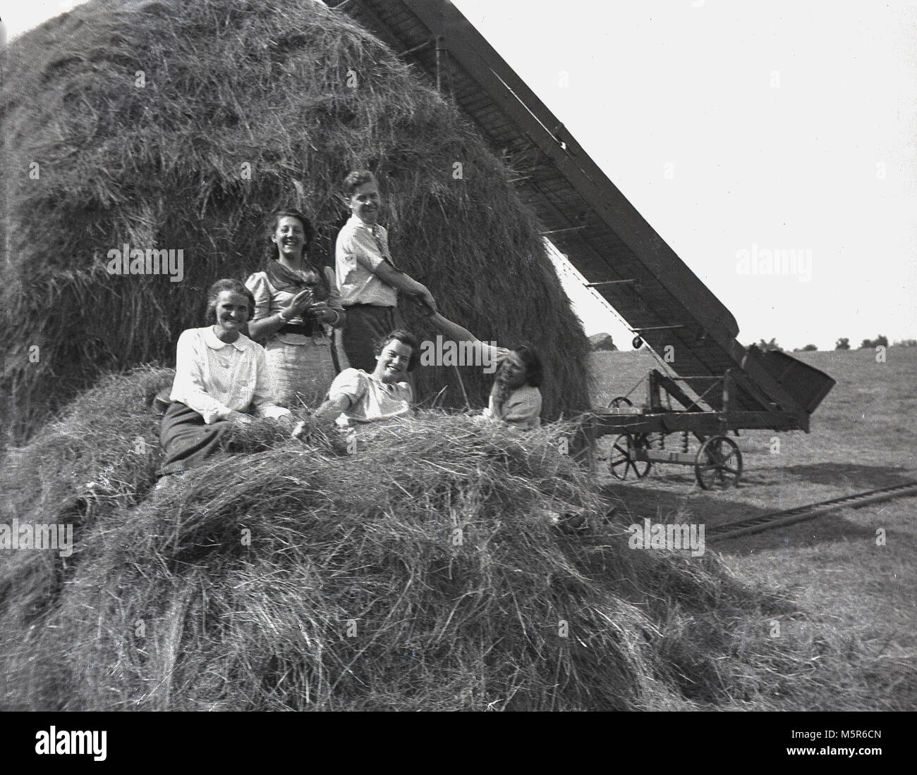 1937, foto storiche, famiglia enoying una vacanza rurale nella fresca aria del Devon, Inghilterra, per divertirsi su un pagliaio su una fattoria di lavoro. Il Pagliaio carrellata di diapositive o di shute può essere visto sulla destra. Foto Stock