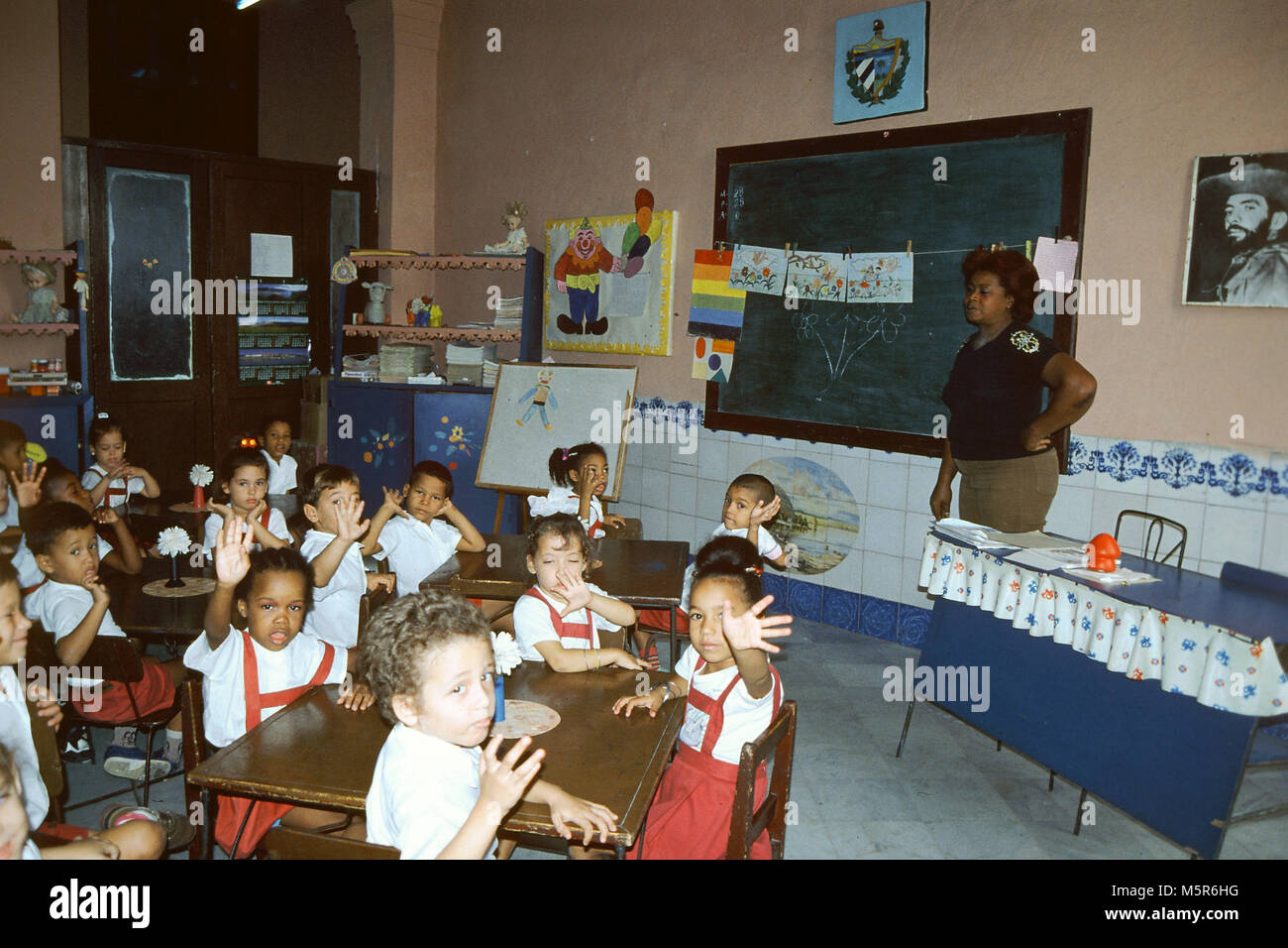 Bambini sventolando in aula in una scuola in Trinidad, Unesco WHS, Cuba.Il ritratto di Camilo Cienfuegos è appeso accanto alla lavagna Foto Stock