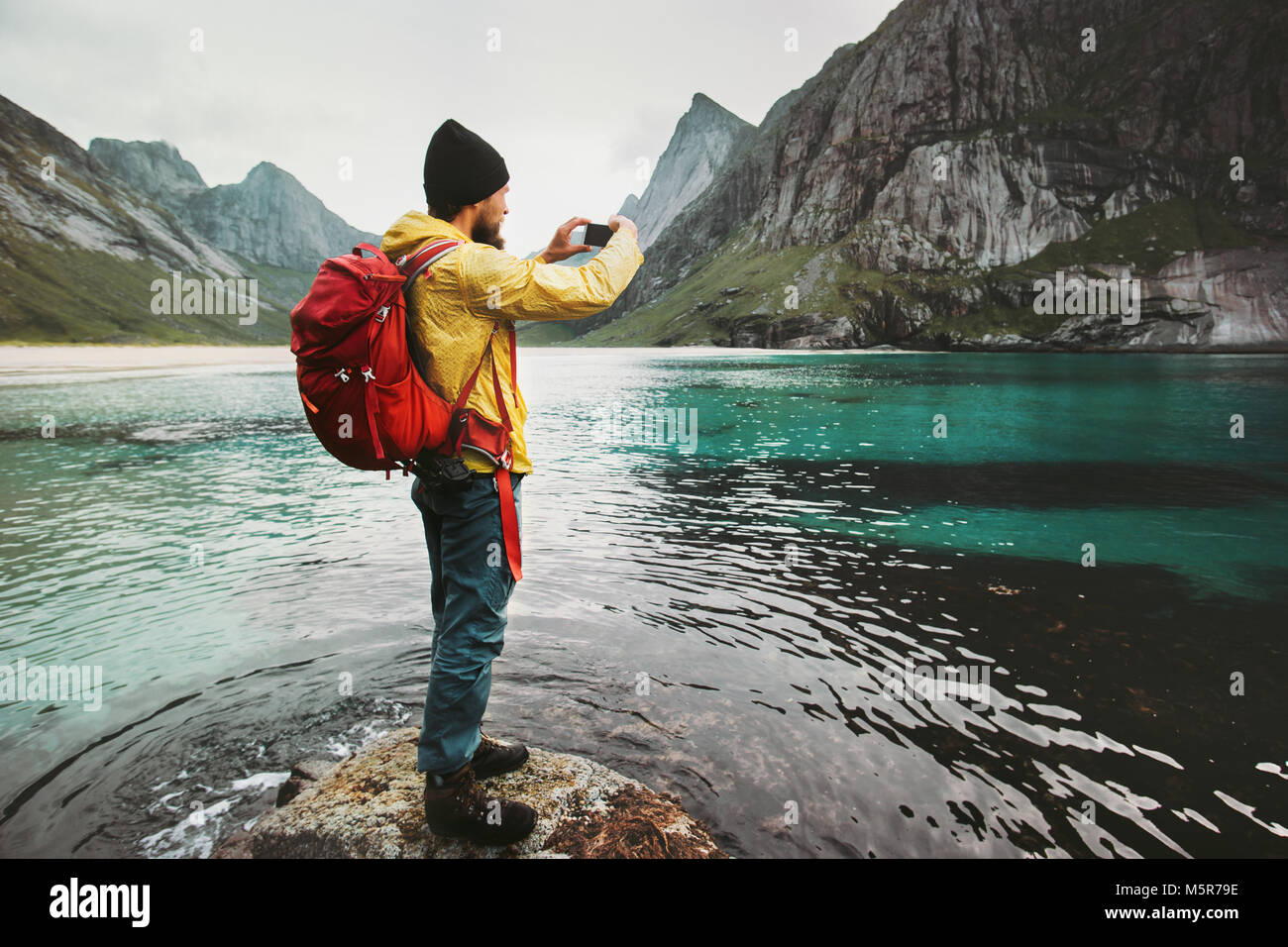 Uomo con zaino prendendo foto tramite smartphone camminando sulla spiaggia di Norvegia Travel lifestyle wanderlust concetto outdoor avventura vacanze estive Foto Stock