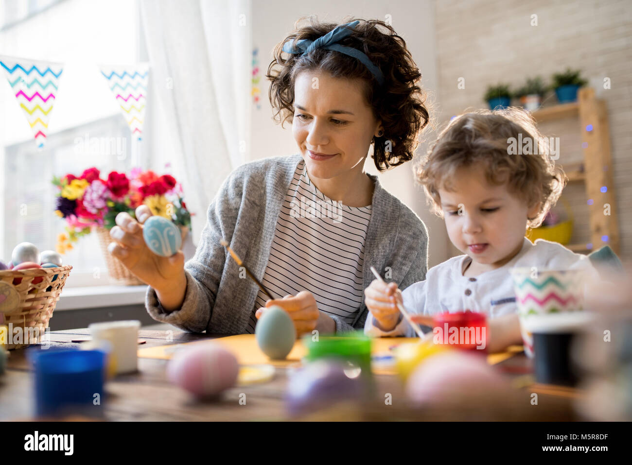 Ritratto di famiglia felice pittura colorata le uova di Pasqua di effettuare decorazioni seduta a tavola a casa Foto Stock