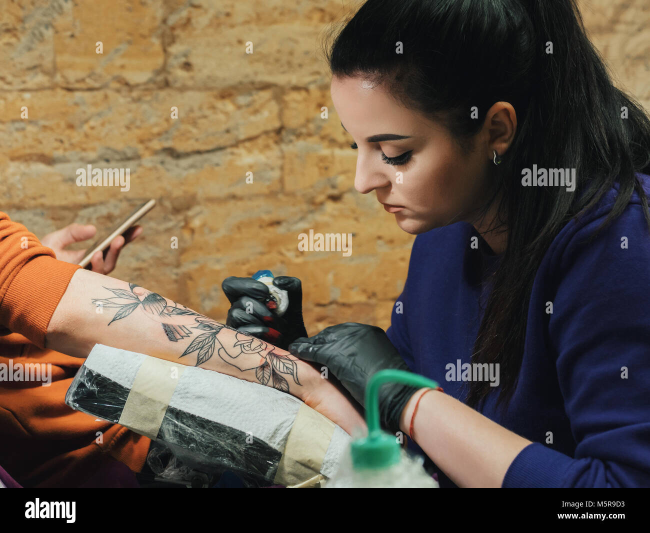 Ritratto di bruna tattooer femmina in viola abbigliamento rendendo tattoo sull'uomo del braccio del suo client con la pistola in studio. Giovane donna di affari in opere Foto Stock