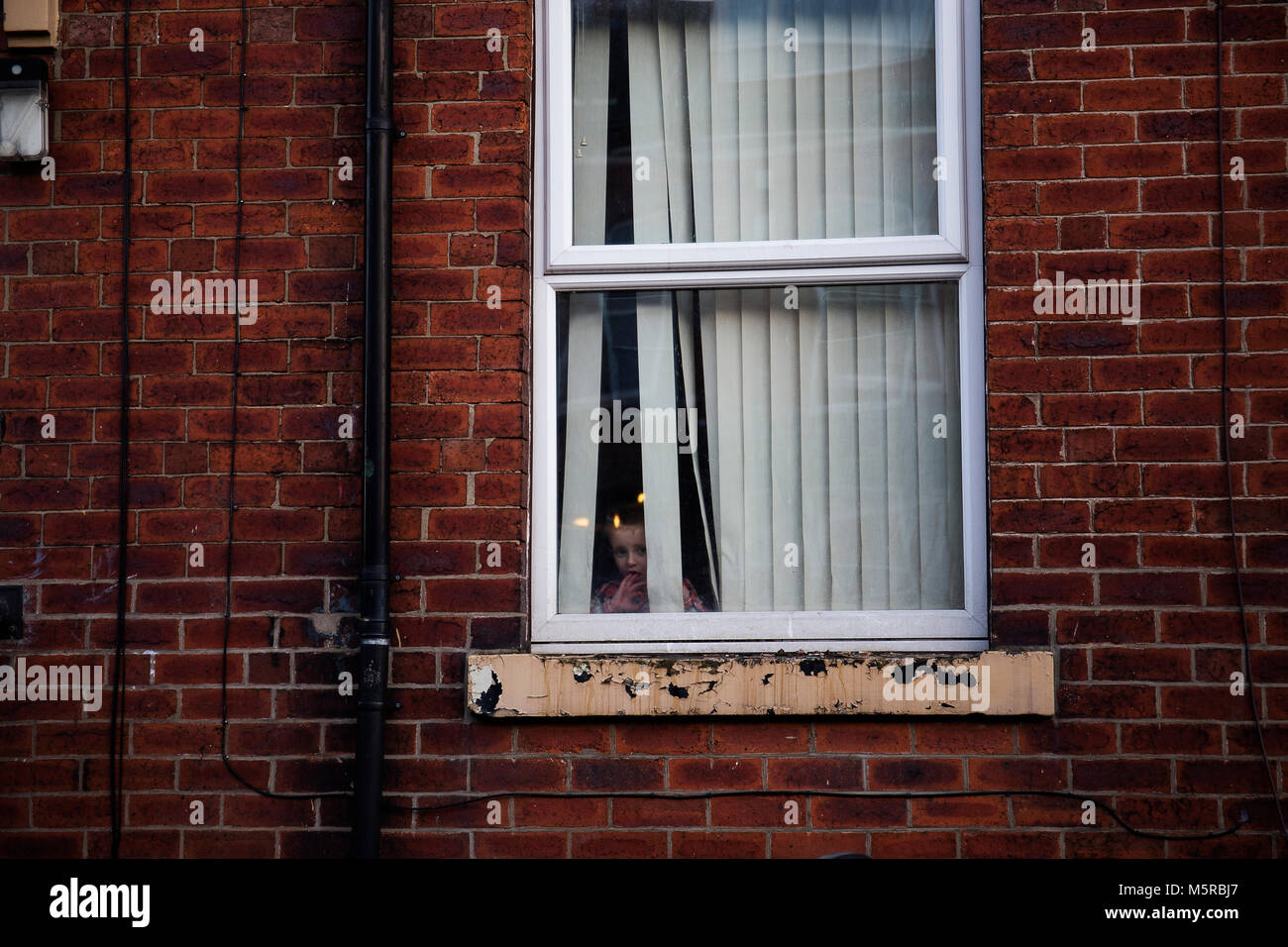 Un bambini all'interno di una casa di guardare fuori dalla finestra. Foto Stock