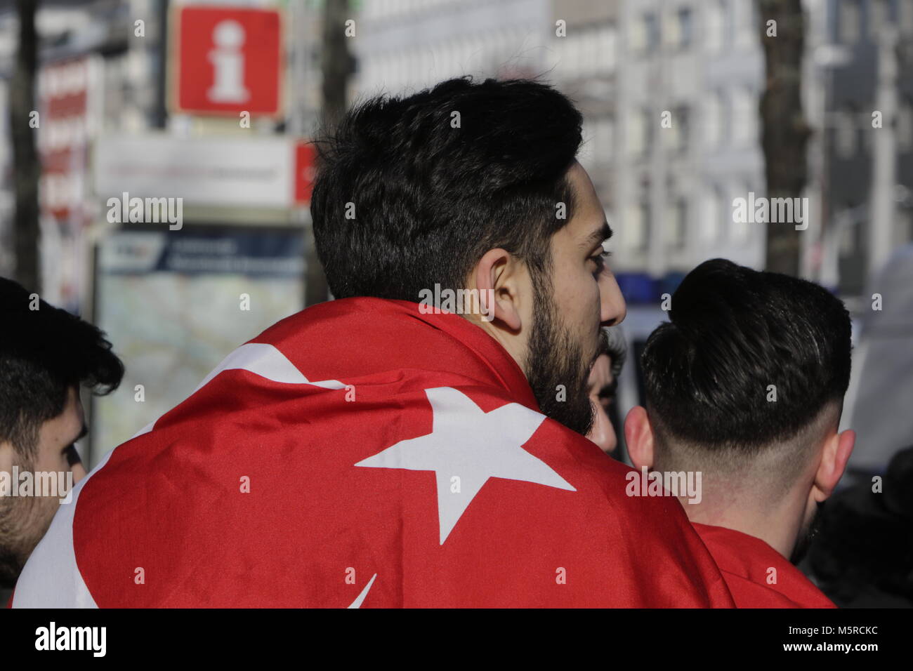 Mannheim, Germania. Il 25 febbraio, 2018. Un manifestante indossa una bandiera turca oltre alle sue spalle. Turchi e curdi manifestanti di fronte gli uni degli altri in occasione delle proteste nel centro della città di Mannheim. Il bagno turco manifestanti hanno sostenuto l'attacco da parte dell'esercito turco sulla città siriana di Afrin, il quale è controllato dal popolare curda Unità di Protezione (YPG). Il contatore curda manifestanti hanno chiesto lo stato turco i terroristi per l'attacco. Credito: Michael Debets/Pacific Press/Alamy Live News Foto Stock