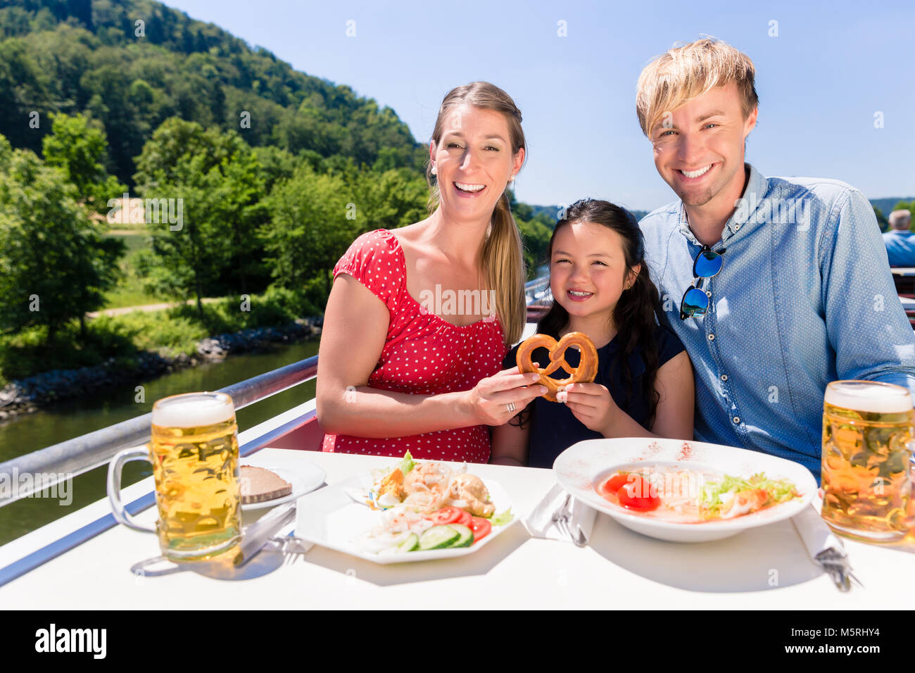 La famiglia a pranzo sulla crociera fluviale con bicchieri da birra sul ponte Foto Stock