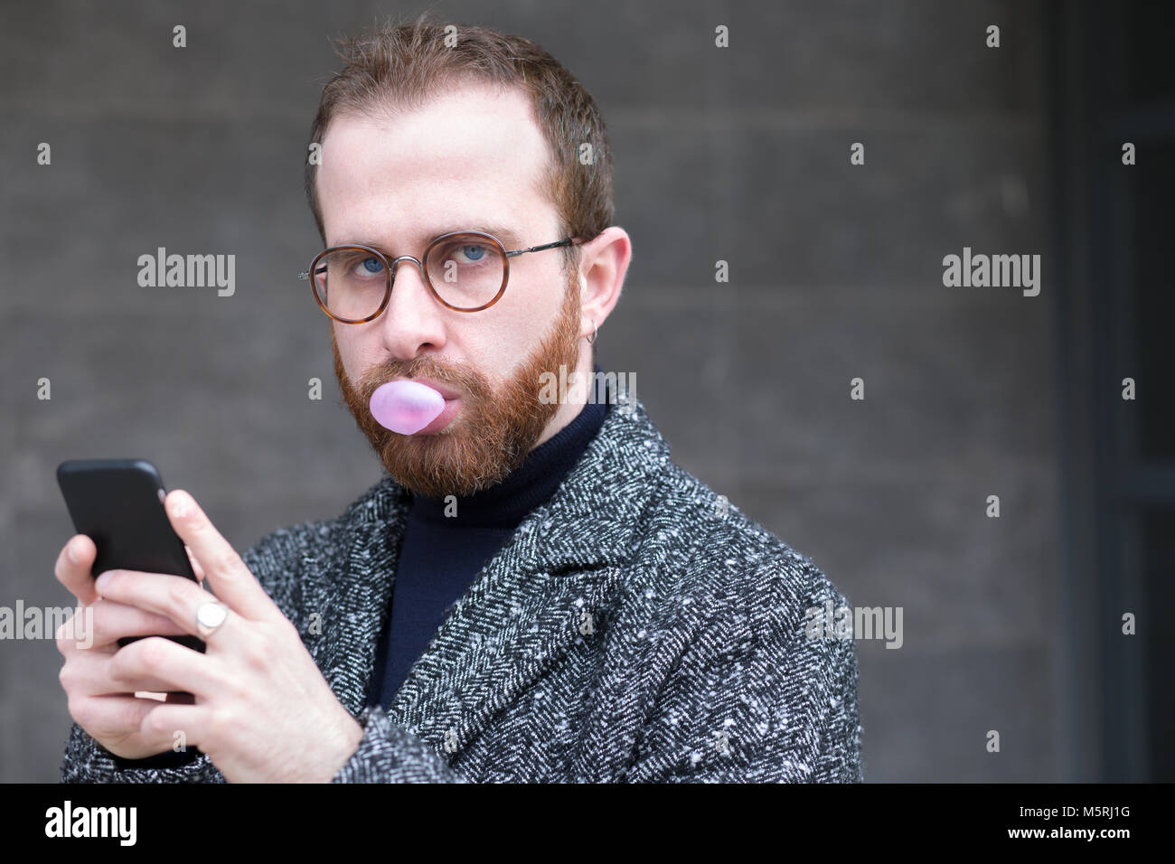 Uomo Barbuto con lo smartphone soffiando una bolla con Bubblegum Foto Stock