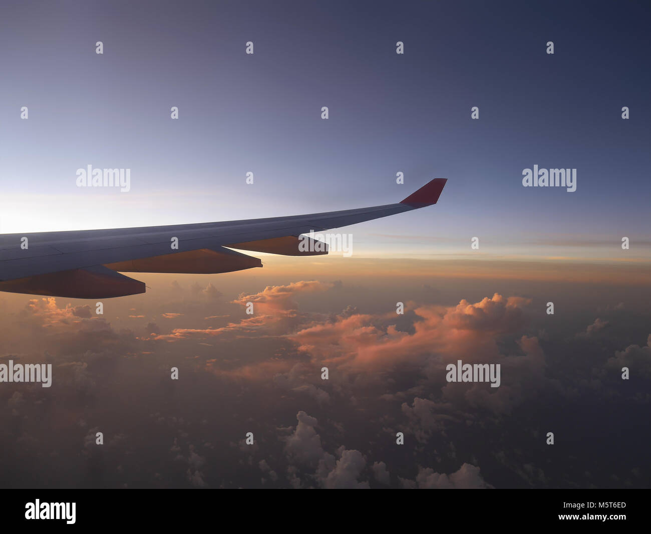 Vista aerea da aereo, vedendo il piano è ala e rosa la luce del tramonto dal lato sinistro, sopra le nuvole orizzonte sotto il cielo blu che si sta oscurando Foto Stock