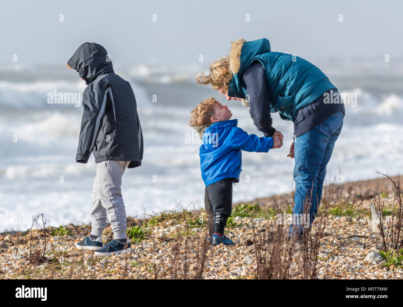 Donna con 2 bambini appaiono essere disciplinare uno di loro su una spiaggia in una fredda giornata ruvida in inverno nel Regno Unito. Foto Stock