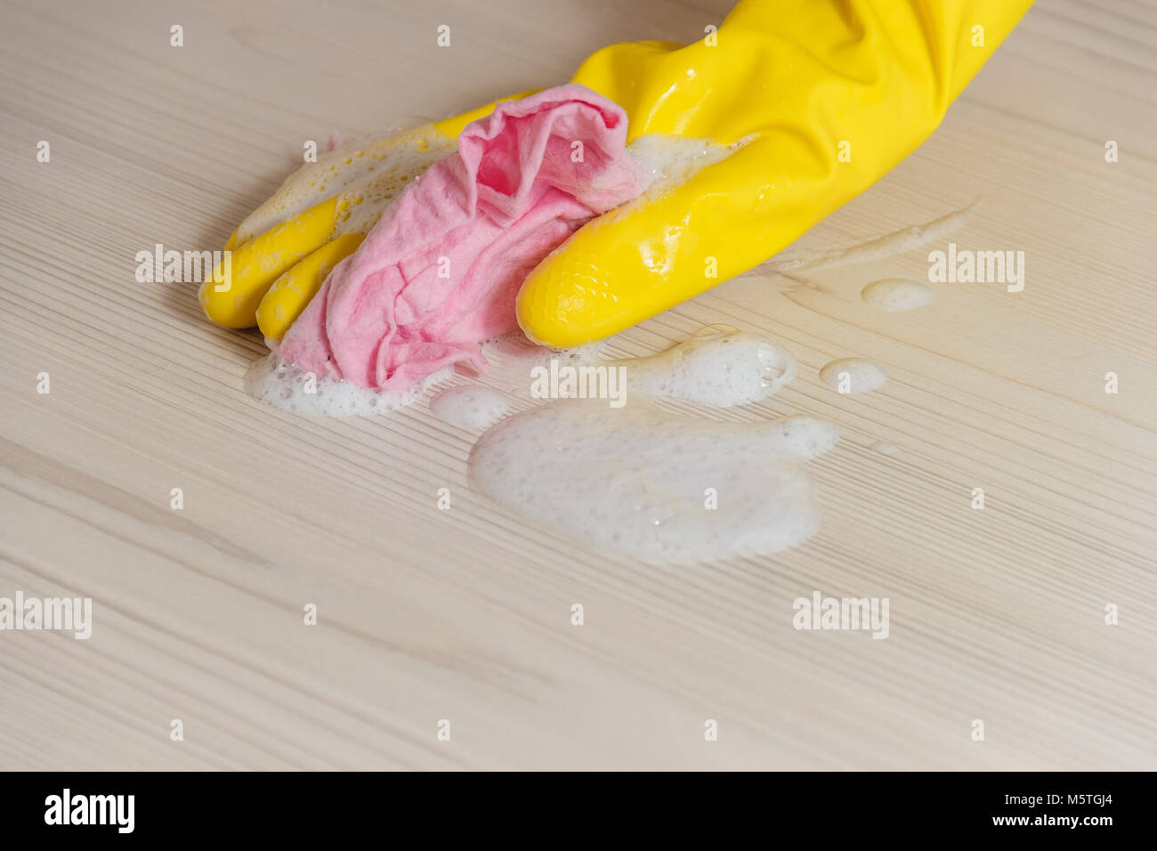 Mano femmina in giallo Guanto di pulizia in legno luce Tavolo moderno con panno di colore rosa per la casa manutenzione e il servizio di pulizie Foto Stock