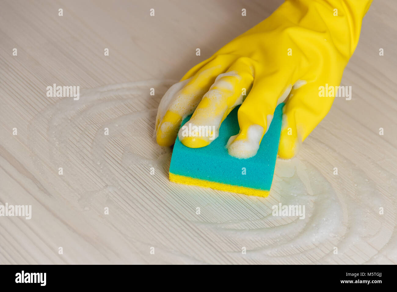 Mano femmina in giallo Guanto di pulizia in legno luce Tavolo moderno con spugna blu per manutenzione domestica e il servizio di pulizie Foto Stock